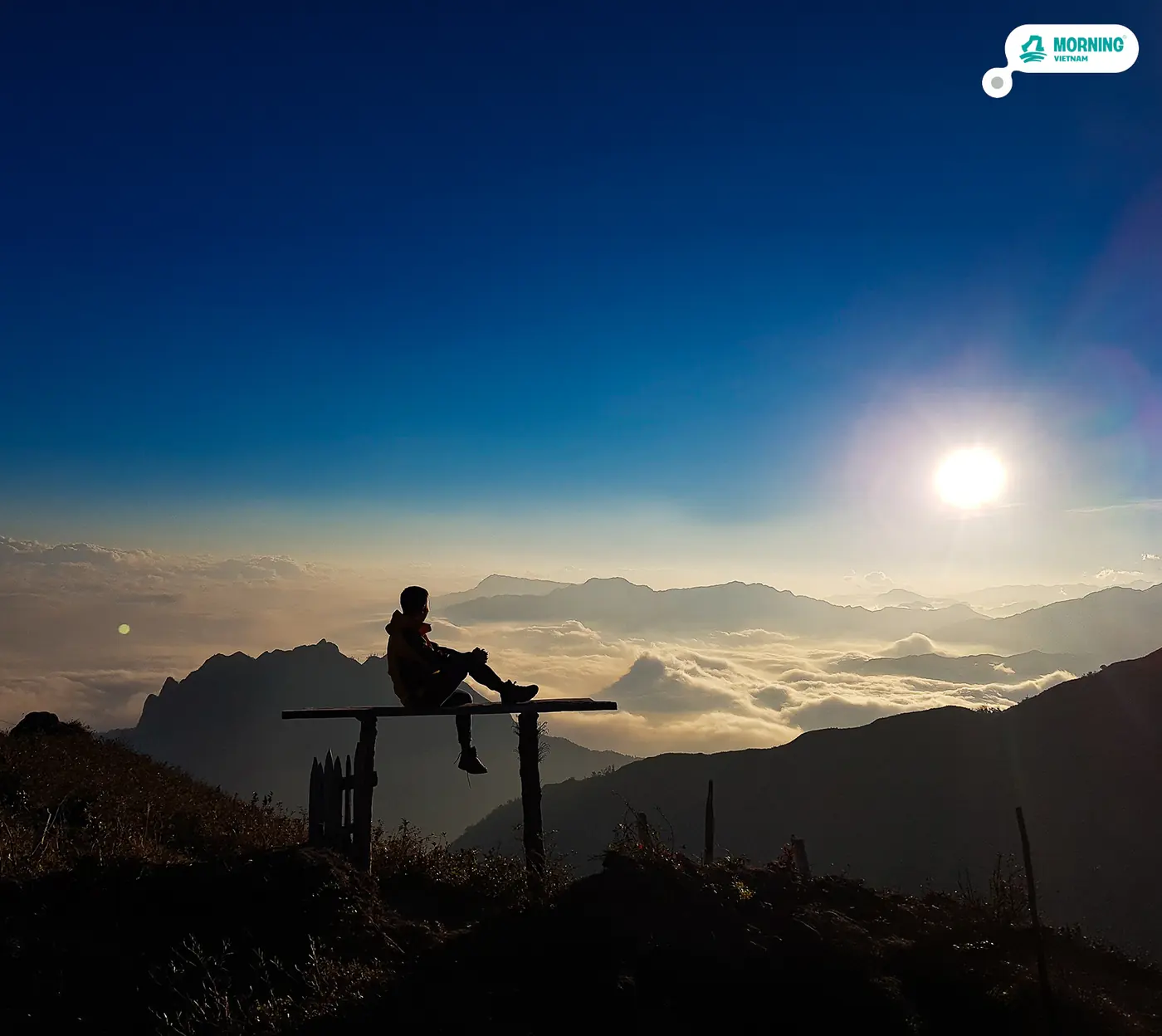 Trekker sitting at a lookout as the sun rises over the clouds