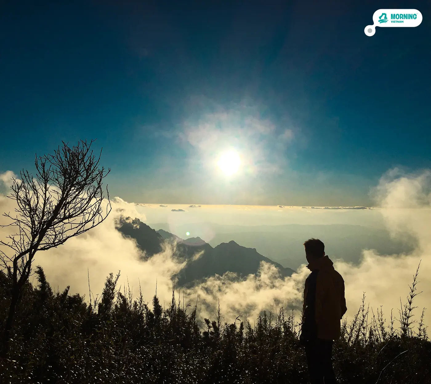 Trekker watching the sun above a cloud-filled valley